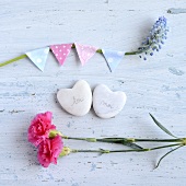Heart-shaped stones with writing on, between pink dianthus flowers and a decorated stem of grape hyacinths