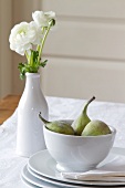 White ranunculus in a white porcelain vase, next to a dish of sweet figs