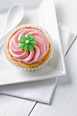 A cupcake topped with pink icing and a green flower