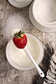 Joghurt mit Erdbeere auf einem Löffel; daneben eine Zuckerdose