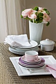 Stacked plates and coffee cups; in the background, a bunch of flowers with pink ranunculus