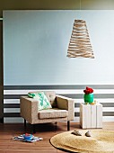 Schwerelose Drahtlampe vor heller Wand und Sockel mit grauen Querstreifen als Hintergrund für gemütlichen Sessel