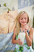 Blondes Mädchen hält ein Glas Milchshake mit zwei Strohhalmen