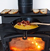 Eggs and Bacon Cooking in a Cast Iron Skillet on a Wood Burning Stove; Bread Toasting on the Stove