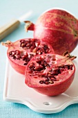 A whole and a halved pomegranate on a chopping board with a knife