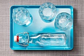 Drei Wassergläser und eine Wasserflasche auf blauem Tablett