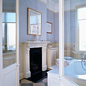 Blick durch offene Flügeltür auf Kamin mit weisser, profilierter Holzschürze in traditionellem Bad mit pastellfarben getönten Wänden
