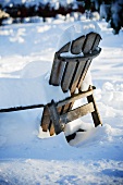 Mit Schnee bedeckter Holzstuhl im Garten
