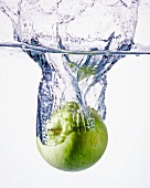 Ein grüner Apfel fällt ins Wasser