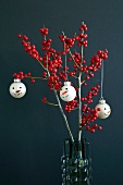 Christmas tree baubles with snowman's faces hanging on branches of red holly berries (ilex)