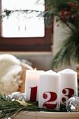 White Advent candles printed with the numbers 1, 2, 3 on plate decorated with fir branches and disco balls