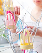 Woman decorating white twigs with paper bird cages