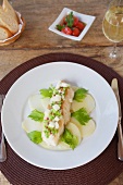 Sea Bass Over Thin Sliced Potatoes on a White Plate; Bread, Cherry Tomatoes and a Glass of White Wine
