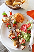 Shrimp and vegetable Skewers with a Side Salad, Rice and Tortilla Chips; On a White Plate