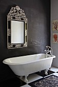 Vintage, claw-footed bathtub on chequered floor against dark wall with framed mirror