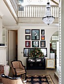 Gallery of pictures above Colonial-style cabinet and antique upholstered armchairs in double-height hall with encircling gallery