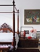 Dark-wood, Colonial-style canopy bed; red ethnic figurine on bedside cabinet and Na