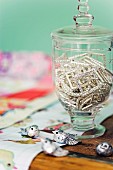 Rhinestone buckles in goblet-shaped, lidded glass jar and small silver bird ornaments