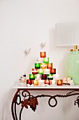 Pyramid of colourful tealight holders next to table lamp on console table