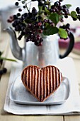 A striped heart-shaped biscuit in front of a bunch of aronia berries
