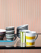 Colourful crockery on glass table in front of red and white striped wall