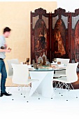 Antikes Paravent vor modernem Esstisch mit Glasplatte und weissen Designerstühlen