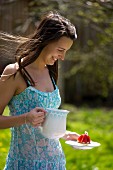 Junge Frau mit Milchkrug und Erdbeertörtchen im Freien