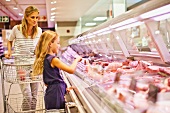 A mother and daughter at the meat counter in a supermarket