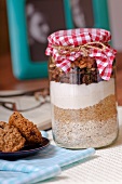 A jar containing dry ingredients for making walnut and oat biscuits with chocolate chips