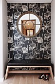 Round, latticed window on floral wallpaper and bench with black leather seat cushion in niche