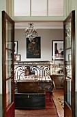 View through open, glass double doors into vintage bedroom with old trunks at foot of ornate, wrought iron bed
