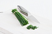 A bunch of chives and a knife on a chopping board