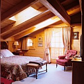 Double bed below skylight and antique armchair next to balcony door in wooden house