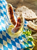 Two grilled bratwurst sausages in a glass with mustard