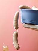 Raw white sausages hanging over the edge of a blue plastic bowl