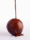 A chocolate ball being coated in glaze