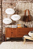 Vintage bag hanging from wooden coat hanger and three, white, designer pendant lamps decorating old brick wall