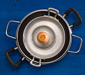 A stack of cookware with a soft-boiled egg in the shell, top cracked open
