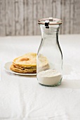 A jar containing the dry ingredient mix for making pancakes and a plate of cooked pancakes