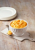 Carrot, swede and potato mash in rustic white bowl with large metal spoon