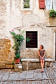 Frau sitzt auf Steinbank vor Haus in Istrien, Kroatien