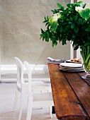 weiße Stühle vor rustikalem Holztisch mit Blumenvase