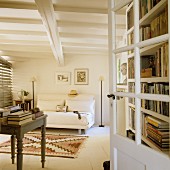 View through open door of rustic table and pale, modern sofa in interior with white wooden ceiling