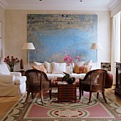 Large, abstract painting behind seating area with loose-covered sofa and classic wicker armchairs in elegant ambiance