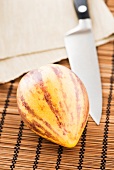 A Pepino melon with a knife on a bamboo mat