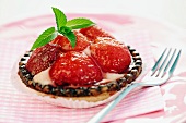 An individual strawberry tart with mint leaves