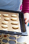 A woman holding a baking tray of uncooked pastry parcels, filled with lentils and tomatoes