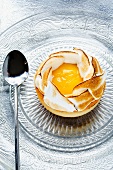 An individual lemon meringue tart and a spoon on a glass plate