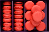 Frisch gebackene rote Macarons in einem lila Karton