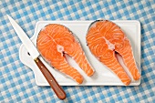 Two fresh salmon steaks on a chopping board with a knife